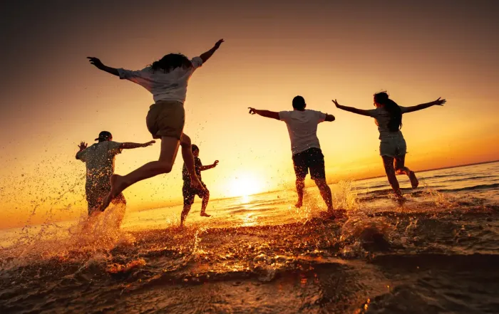 Group of happy young friends run and jump at sunset beach