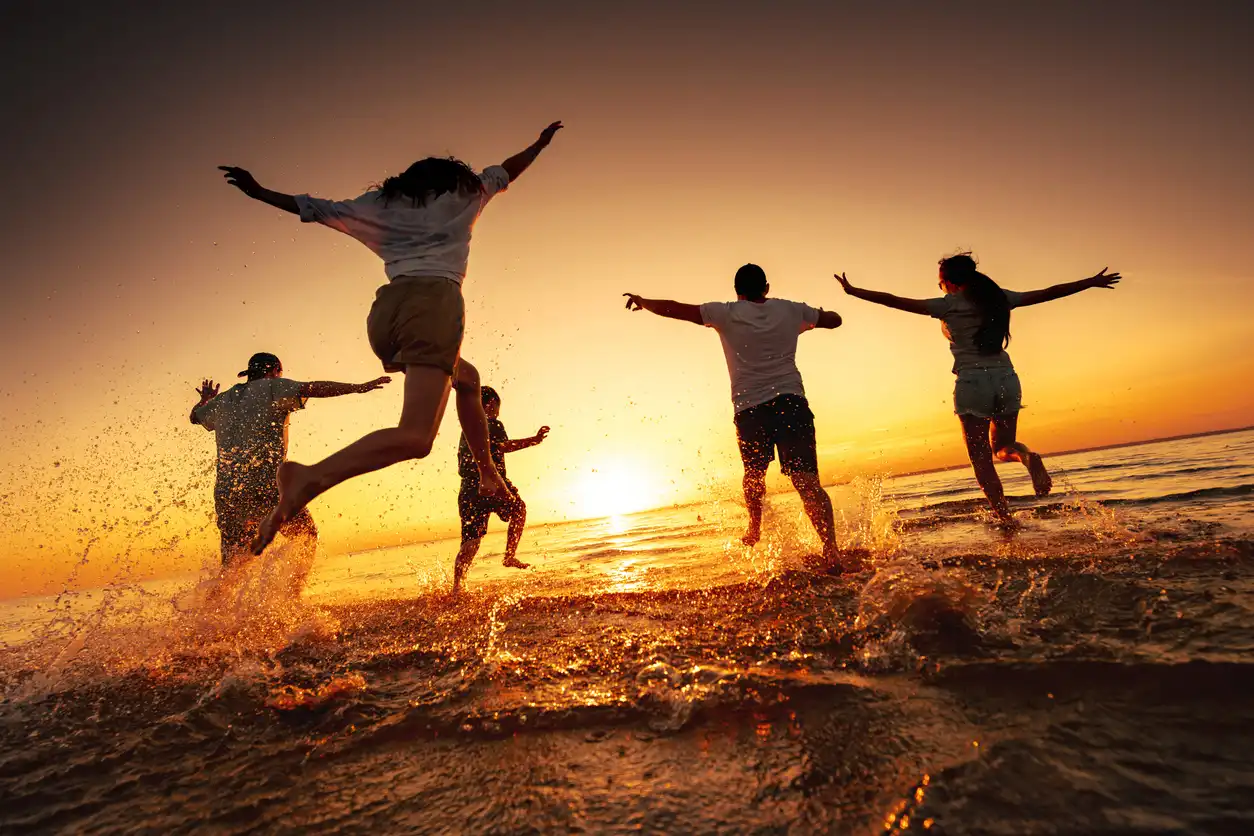 Group of happy young friends run and jump at sunset beach